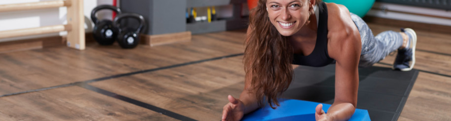 Frau in einem Fitnessraum macht auf einer Fitnessmatte mit einem Balance Pad eine Plank