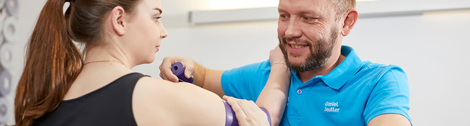 Therapeut hilft seiner Patientin bei der Rehabilitation vom Arm mit Fazienrollen